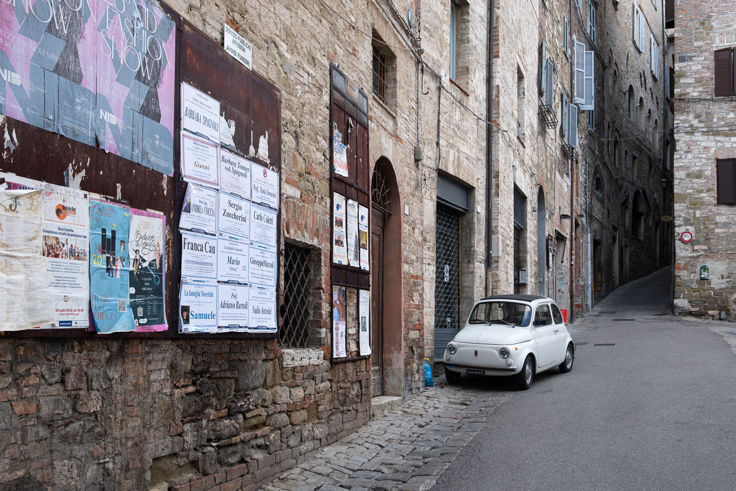 Weißer Fiat 500 in der Gasse – Plakatwand mit Todesanzeigen